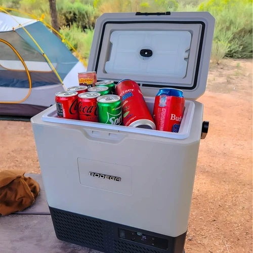 BODEGACOOLER portable car refrigerator filled with canned drinks at an outdoor campsite.