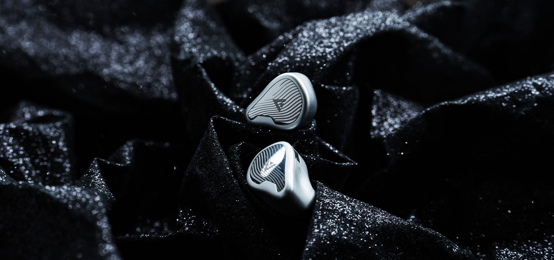 Silver in-ear monitors displayed on dark textured fabric