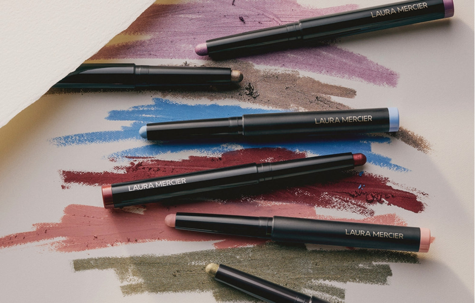 Laura Mercier Caviar eye shadow sticks arranged over colorful swatches