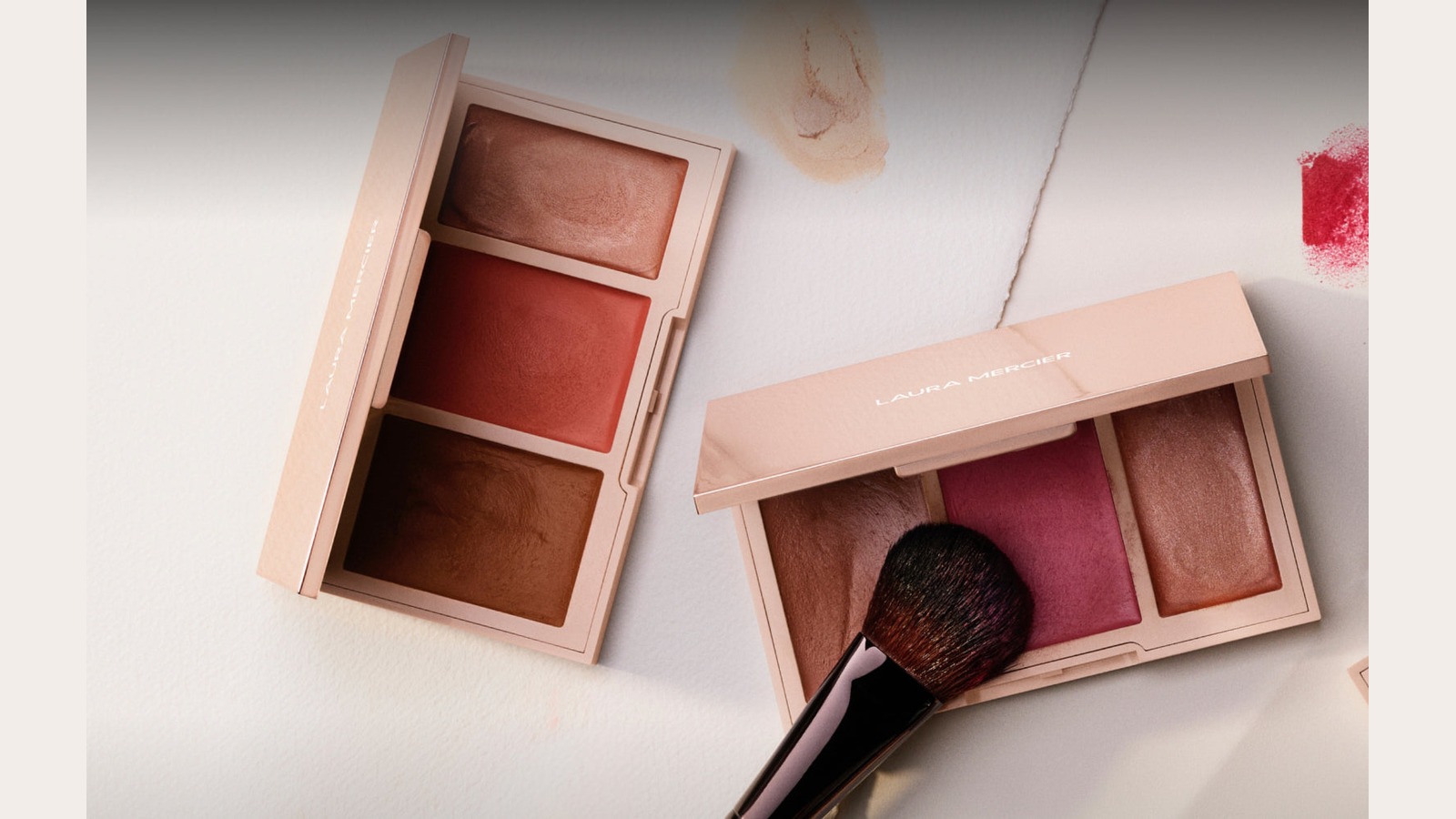 Laura Mercier face palettes and makeup brush arranged on a light surface