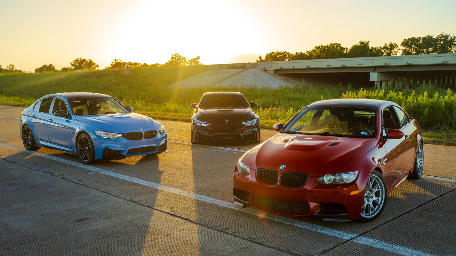 Three modified BMW M cars parked together at sunset