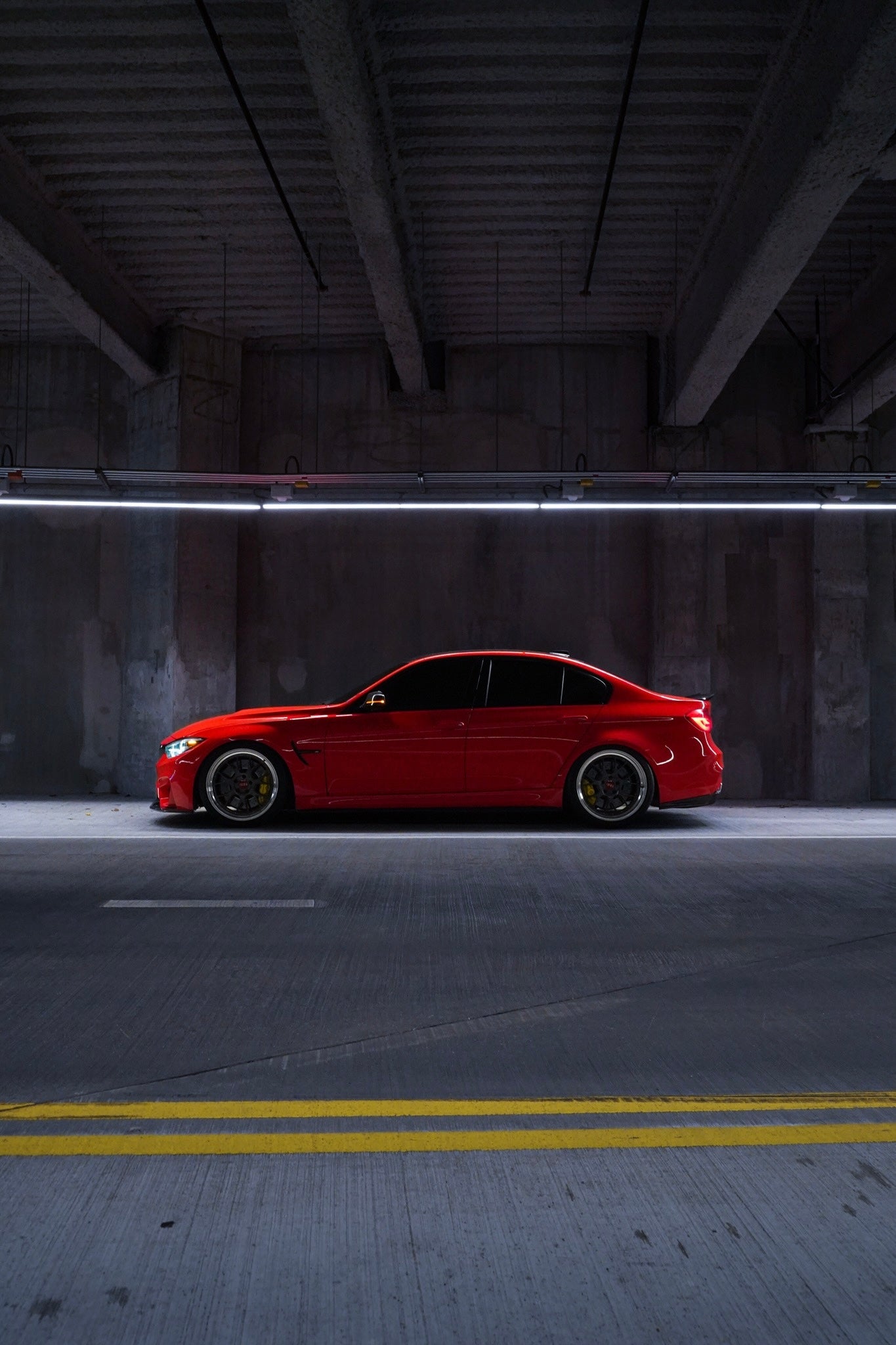 Red BMW M3 sedan photographed in profile in an underground garage